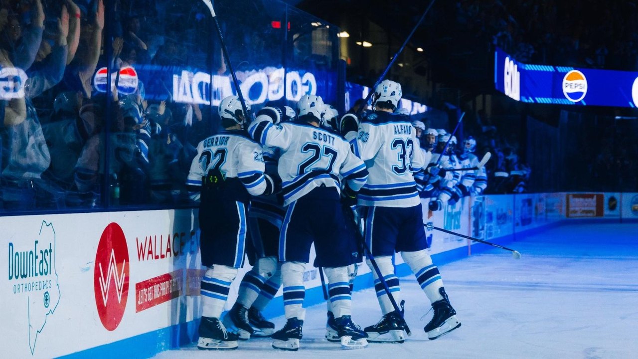 Maine men’s hockey players gather in celebration on the ice.